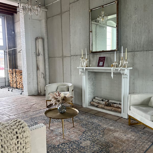 A cozy lounge area with white armchairs, a gold coffee table, and a fireplace with birch logs.