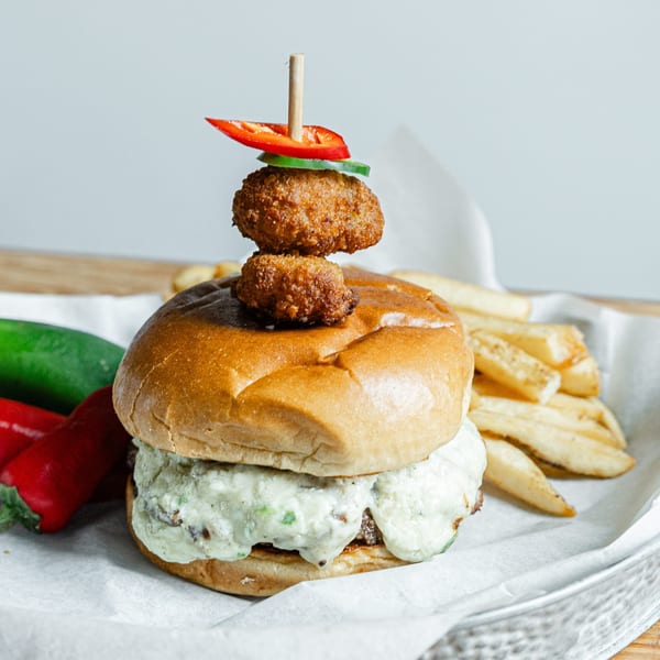 Notch 8 burger with creamy sauce, fried toppings, and fries, garnished with red and green peppers.