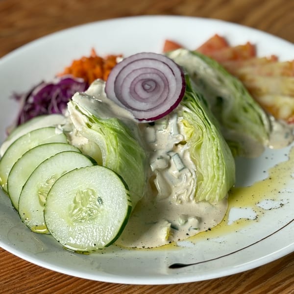 Wedge salad with blue cheese dressing, red onion, cucumbers, and shredded carrots on a white plate.