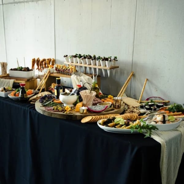 A long table with a black tablecloth is laden with a variety of appetizers and snacks.