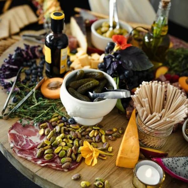 A charcuterie board with meats, cheeses, fruits, nuts, pickles, and bottles of oil and vinegar.