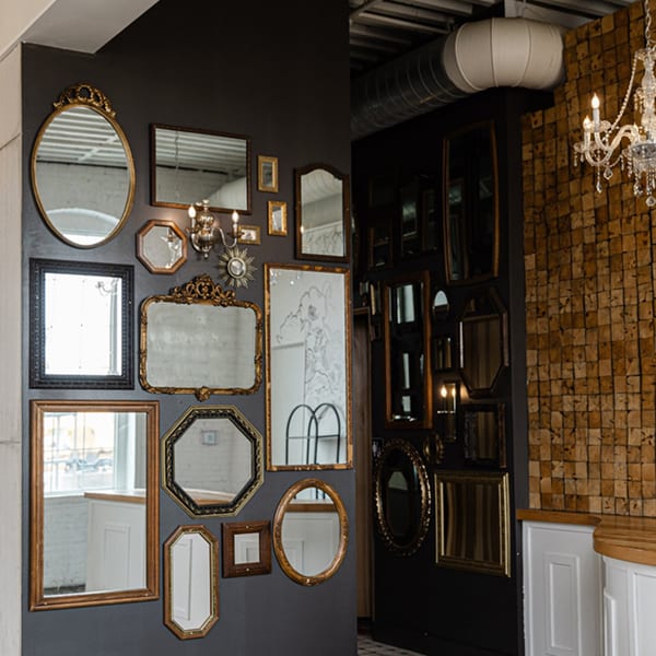 A dark wall covered in an eclectic arrangement of mirrors with ornate gold and black frames.
