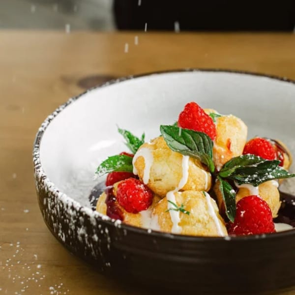 Powdered sugar being sprinkled over Notch 8's dessert with raspberries, cream, and mint.