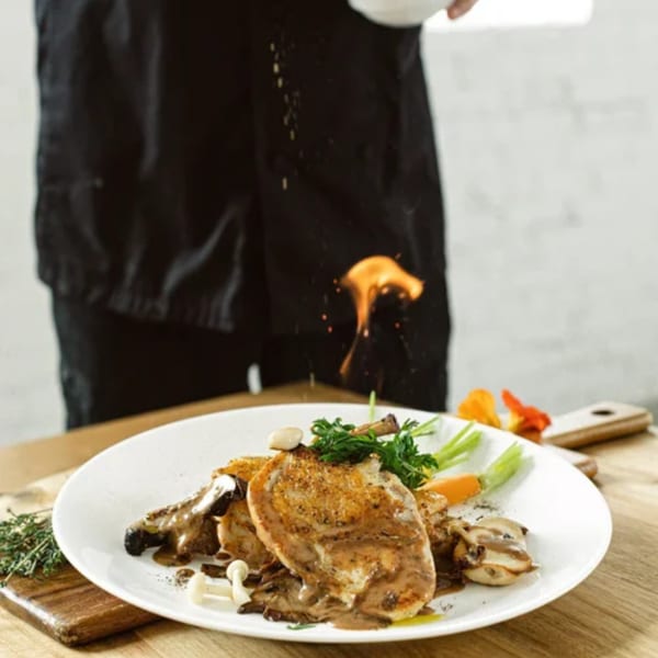 Chef flambéing a Notch 8 American cuisine dish with chicken, mushrooms, and vegetables.