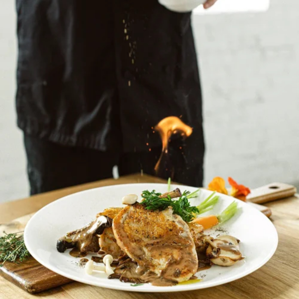 Chef flambéing a Notch 8 American cuisine dish with chicken, mushrooms, and vegetables.
