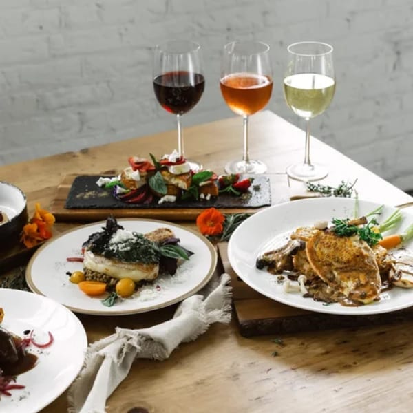 Three gourmet American dishes and three glasses of wine on a rustic wooden table.