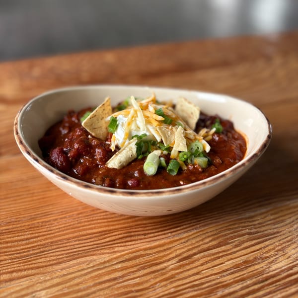 A bowl of Notch 8 chili topped with sour cream, shredded cheese, green onions, and tortilla chips.