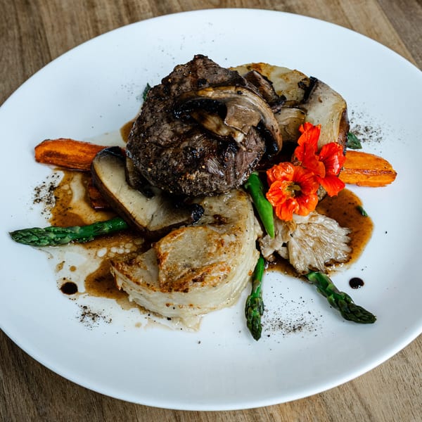 Notch 8's American cuisine: steak with mushrooms, asparagus, carrots, and edible flowers on a white plate.