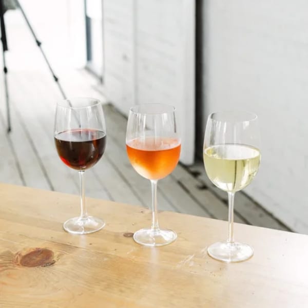 Three wine glasses on a wooden table, filled with red, rosé, and white wine.