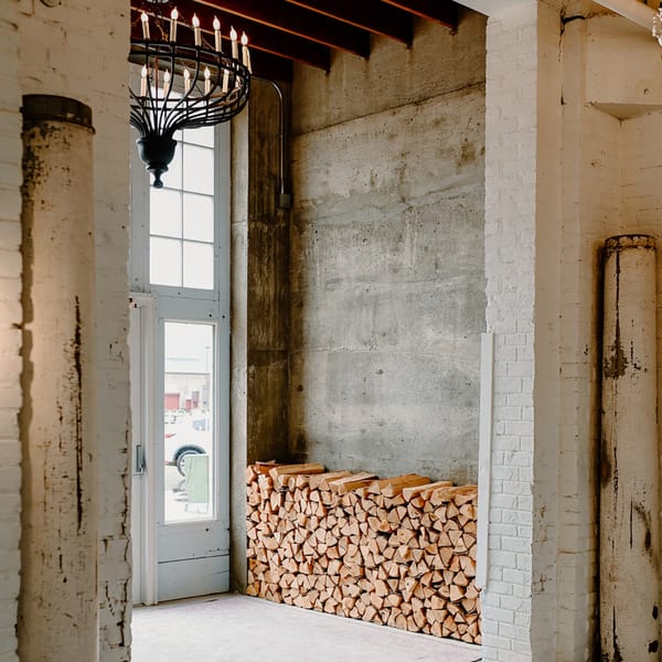 A rustic interior with a large stack of firewood, a white door, and a chandelier.